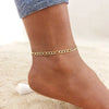A close-up of a woman's ankle wearing a gold stainless steel chain anklet.