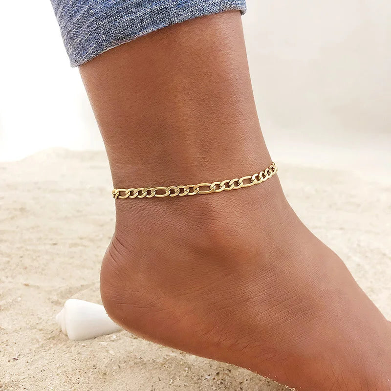 A close-up of a woman's ankle wearing a gold stainless steel chain anklet.