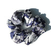 A close-up of luxury pure silk hair scrunchies in shades of gray and deep blue floral patterns.