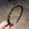 A hand holds a black elastic hair hoop adorned with sparkling rhinestones and small purple stones.