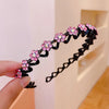 A hand holds a black elastic hair hoop decorated with pink and purple rhinestones shaped like flowers.