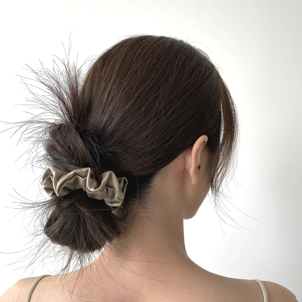 A woman's dark hair is styled in a messy bun with a silk scrunchie, shown from the back.