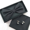 A black bow tie and cufflinks set displayed in a black presentation box and velvet pouch.
