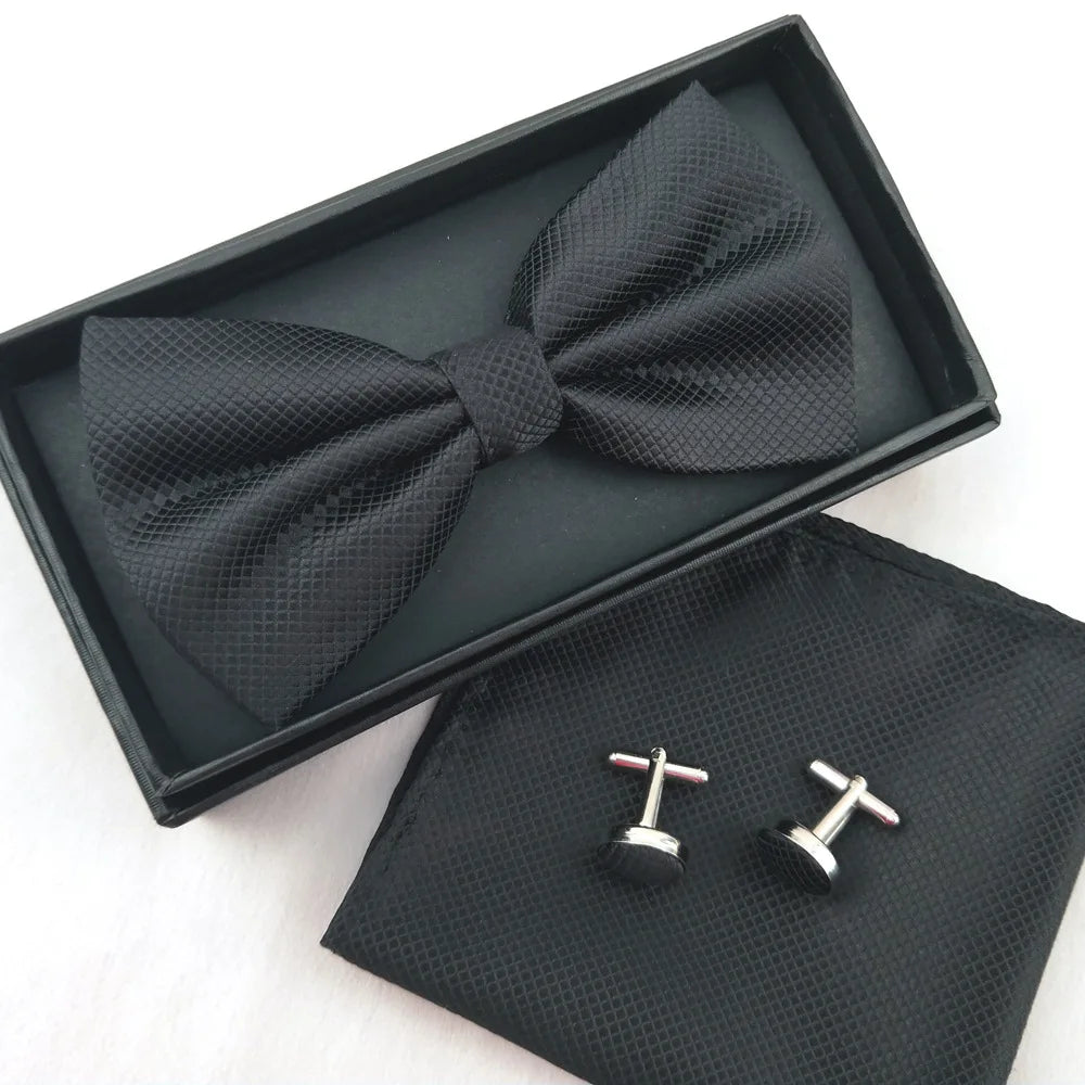 A black bow tie and cufflinks set displayed in a black presentation box and velvet pouch.