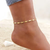 A close-up of a woman's ankle wearing delicate gold stainless steel anklets.