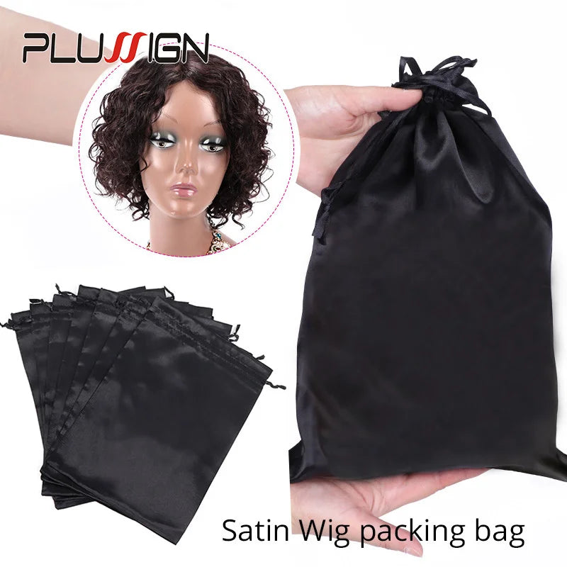 Eine schwarze Satin-Perücke in einer Verpacktasche neben einer Ansammlung gefalteter schwarzer Satinbeutel.