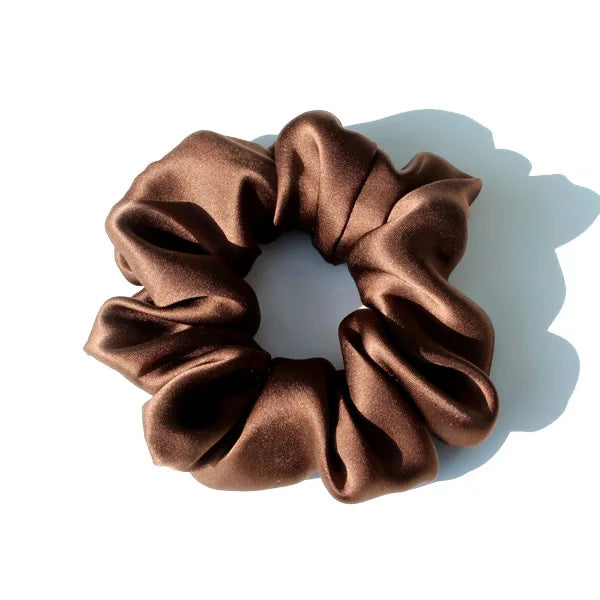 A dark brown satin scrunchie tied in a bow shape, showing luxurious fabric texture.