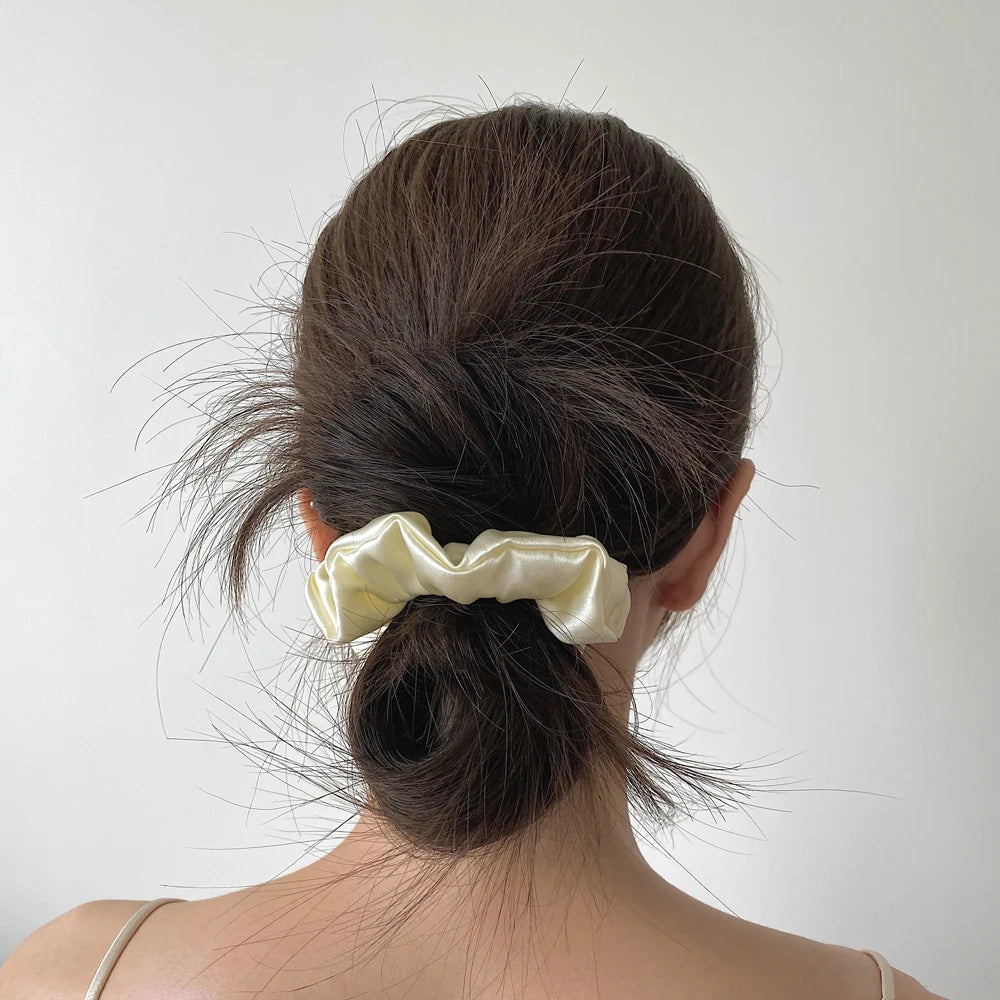A woman's dark hair is styled in a high ponytail with a pale yellow silk scrunchie.