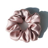 A circular wreath of pink satin fabric forming a scrunchie, shown in soft light.
