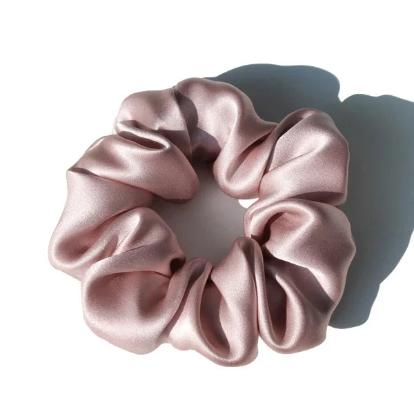 A circular wreath of pink satin fabric forming a scrunchie, shown in soft light.