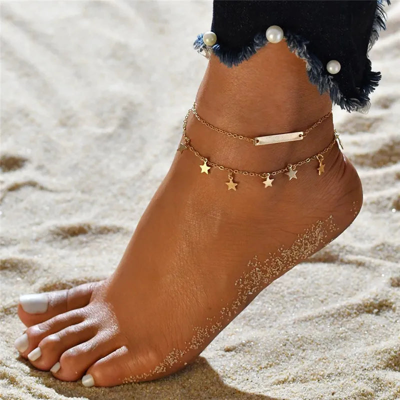 Gold and silver heart chain anklets worn on a foot in sand