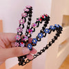 A hand holds a black elastic hair hoop decorated with pink and blue rhinestones.