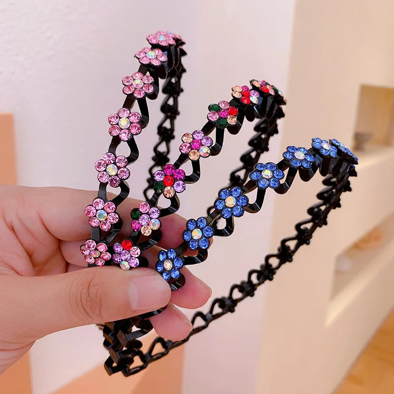 A hand holds a black elastic hair hoop decorated with pink and blue rhinestones.