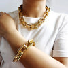 A close-up of a gold boho punk twisted link necklace worn around the neck and wrist against a white shirt.