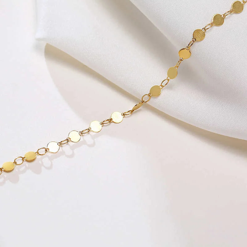 A delicate gold stainless steel anklet featuring small round links, shown against a white fabric background.