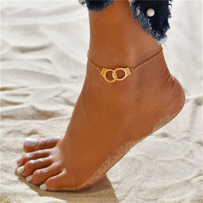 Gold heart chain anklets worn on a foot in a sandy beach setting