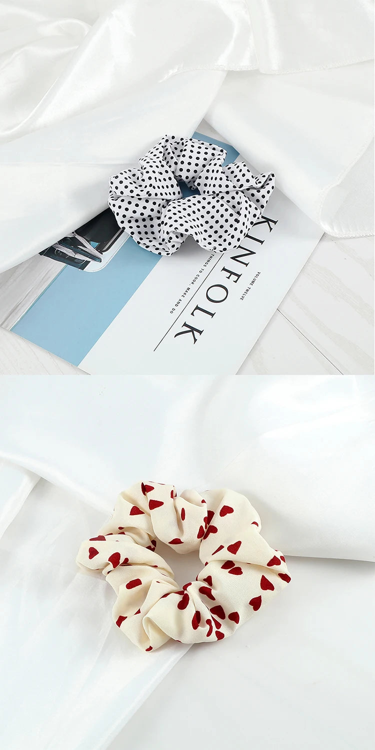 A close-up of a knitted fabric scrunchie headband in cream and red floral pattern resting on white fabric.