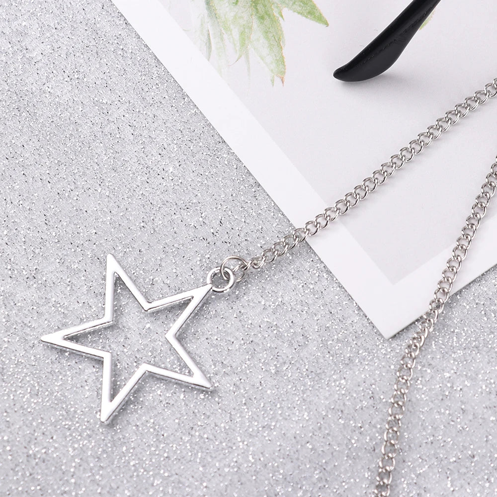 Silver star pendant on a chain resting on a white card against a sparkly gray background.