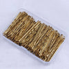 A clear plastic container filled with numerous thin, gold-colored metal hair clips.