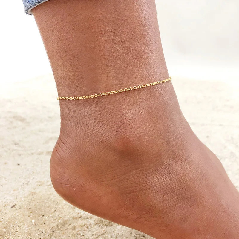 A close-up of a gold stainless steel anklet worn on a woman's ankle.