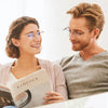 A woman smiling while reading a book, next to a man wearing progressive multifocus reading glasses.