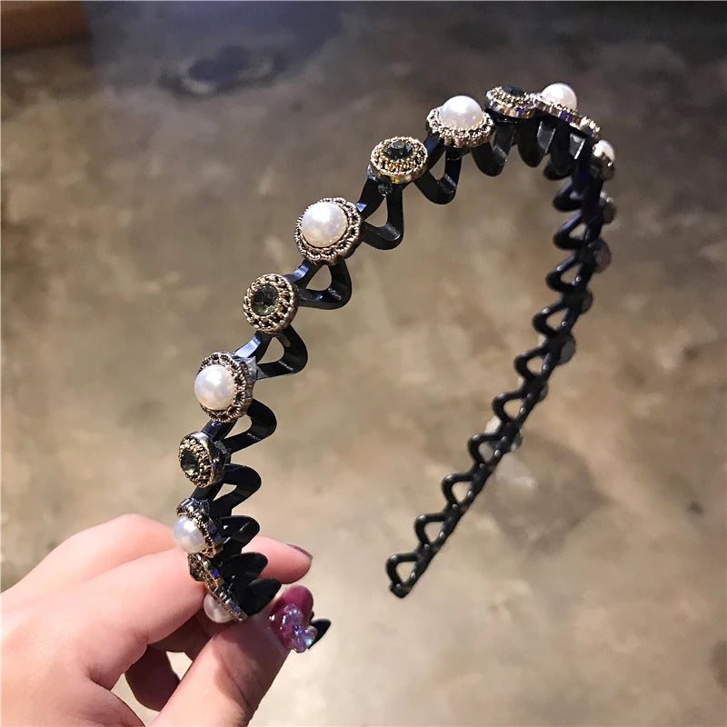 A hand holds a black elastic hair hoop adorned with silver and clear rhinestones.