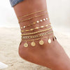 A close-up of a woman's ankle displaying multiple layered gold stainless steel anklets.