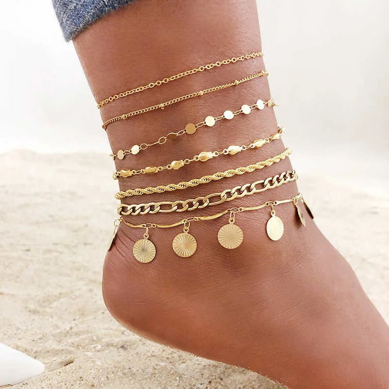 A close-up of a woman's ankle displaying multiple layered gold stainless steel anklets.