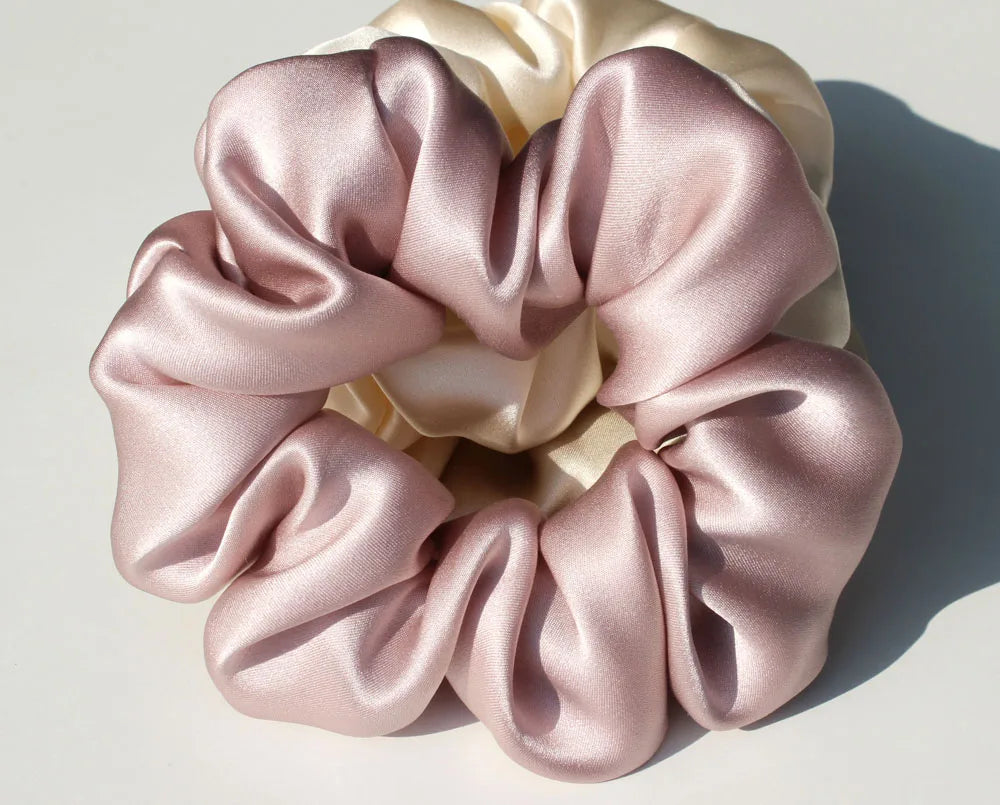 A close-up of luxury pure silk hair scrunchies in soft pink and cream colors, gathered in a rosette shape.