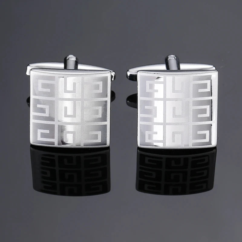 A pair of silver square cufflink holders with a geometric pattern displayed on a dark reflective surface.