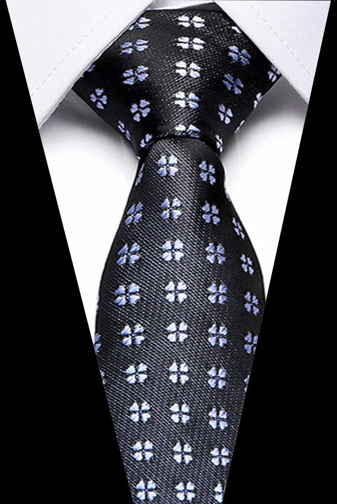Black silk jacquard tie with small blue floral pattern shown against a white shirt.