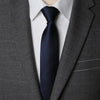 A close-up of a dark blue patterned tie worn under a gray suit jacket and white shirt.