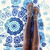 A close-up of a woman's feet and ankles adorned with intricate blue and white beaded tassel anklets.