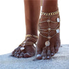 Close-up of a foot adorned with multiple gold chain and silver tassel anklets