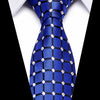 A close-up of a royal blue silk jacquard tie with a white geometric pattern worn against a white shirt.