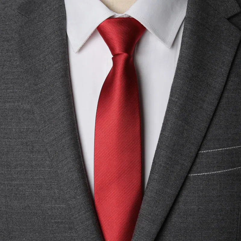 A close-up of a red striped tie worn under a white collared shirt and gray suit jacket.