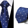 A dark blue silk jacquard tie shown folded and laid flat, featuring a repeating geometric pattern.