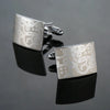 Silver square cufflinks with an engraved swirling pattern displayed on a black surface.