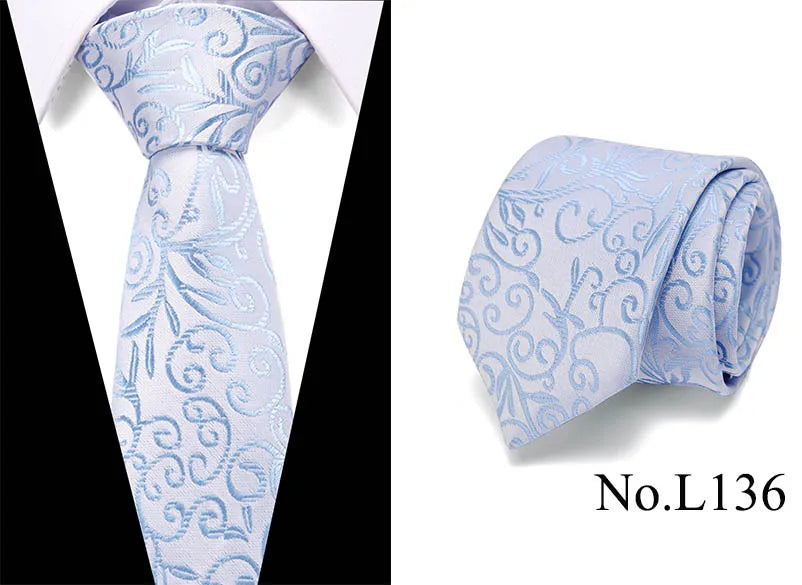 Light blue silk jacquard tie with intricate scrollwork pattern folded and displayed on a white shirt collar.