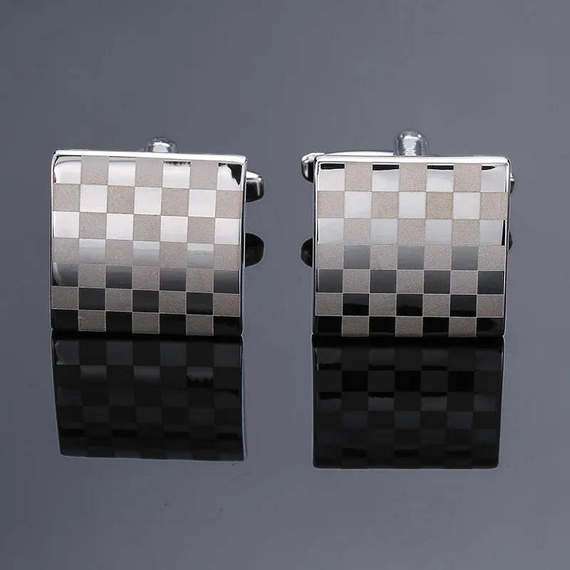 A pair of silver-toned square cufflinks with a checkered pattern, displayed against a dark gray background.