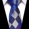 A men's silk jacquard tie featuring a blue, silver, and purple diamond pattern worn against a white shirt.