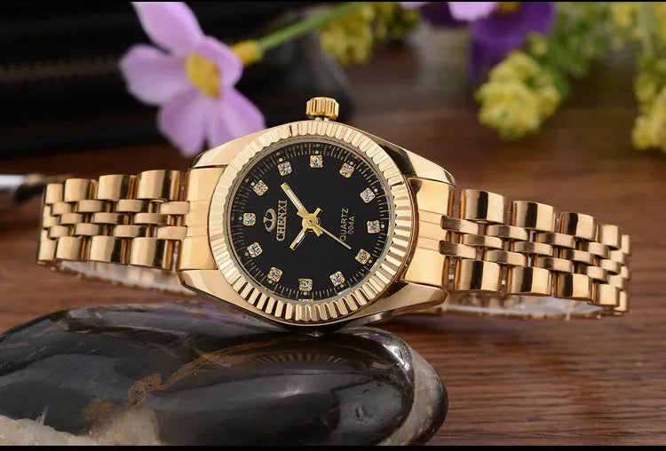 A luxury golden quartz wristwatch with a gold-tone bracelet rests on a dark stone surface.
