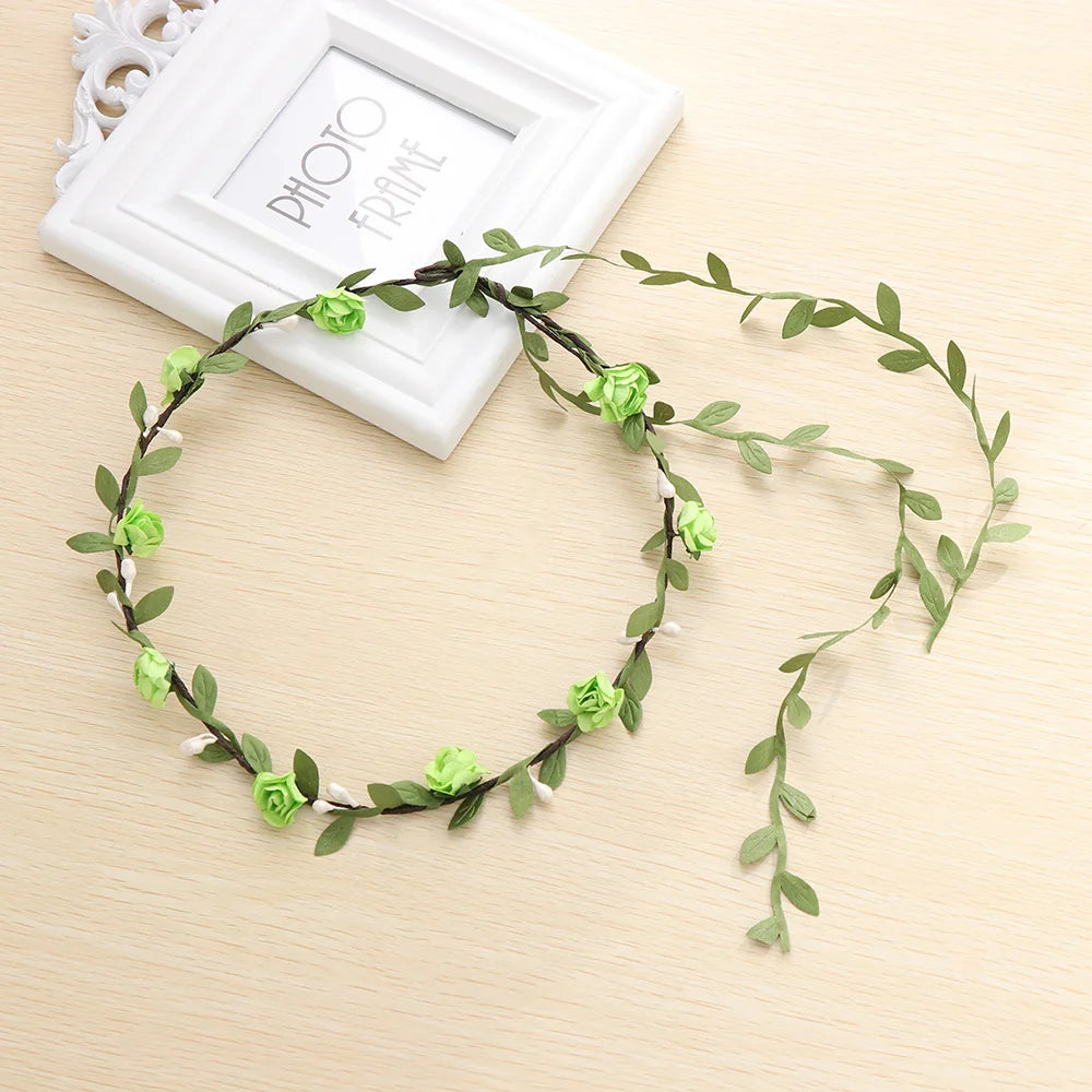 A green floral wreath headband is displayed next to a white photo frame on a light wooden surface.