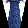 A close-up of a blue silk jacquard tie worn against a white shirt.