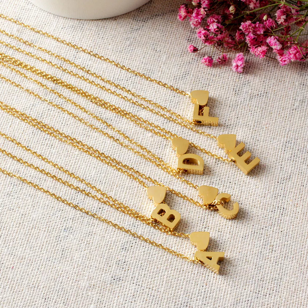 Goldene Initialen-Herz-Kette mit mehreren Strängen auf weißem Leinenhintergrund
