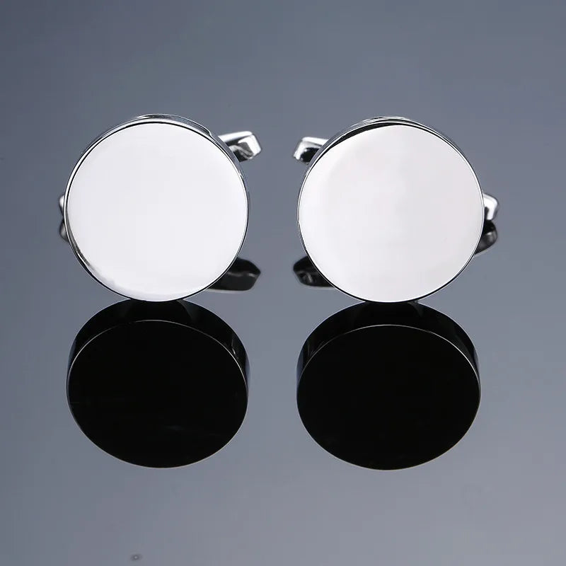 A pair of silver cufflinks with round, polished surfaces displayed against a dark background.