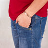 A close-up of a hand wearing a pure copper magnetic bangle with a plum flower design on a denim shirt sleeve.