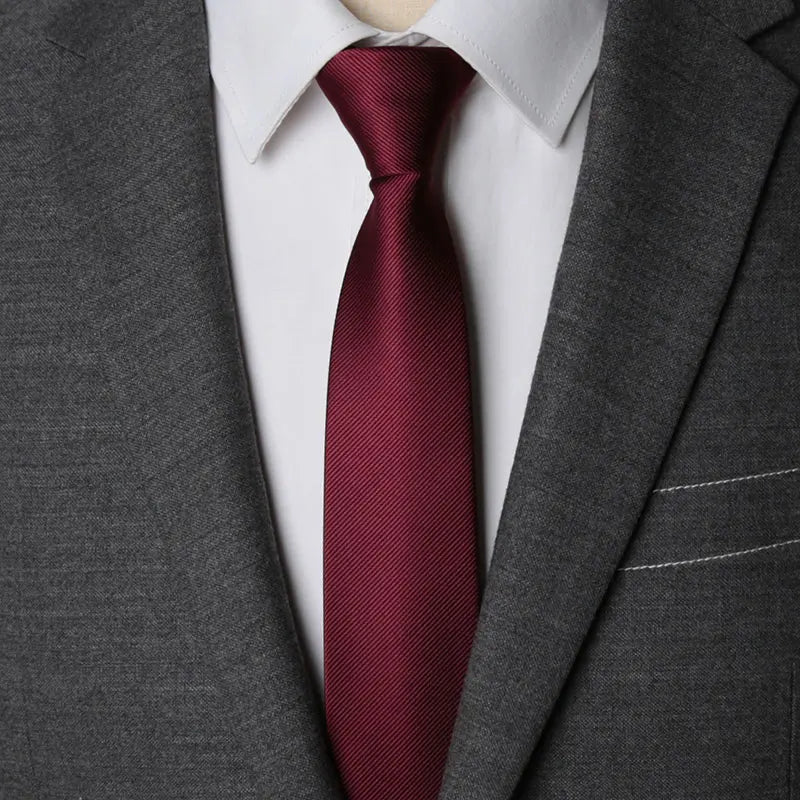 A close-up of a maroon patterned tie worn under a white shirt and gray suit jacket.