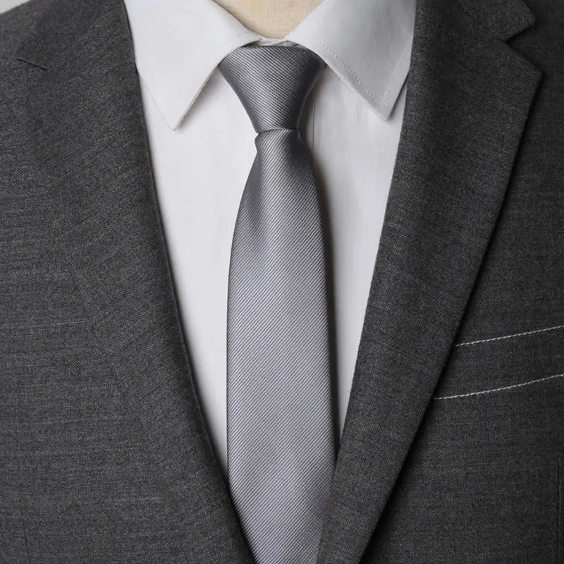 A close-up of a gray striped tie worn under a white collared shirt and dark gray suit jacket.