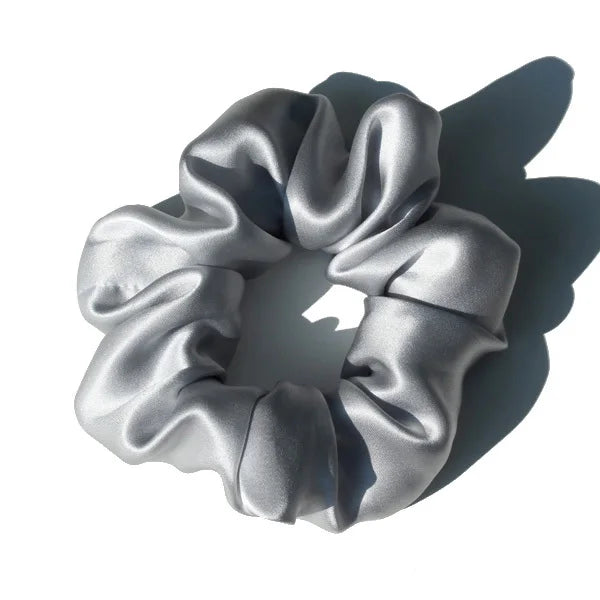 A silver silk hair scrunchie tied in a bow, shown against a white background.
